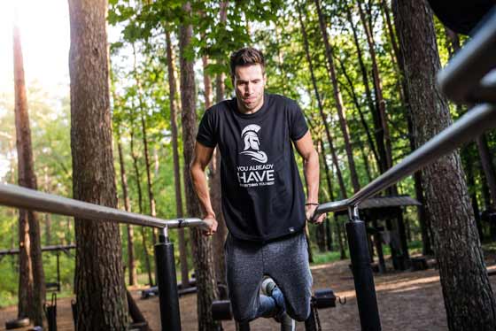 A man working out on parallel bars in a forest setting.