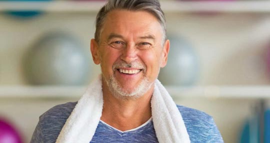 An older man smiling and energized while at a gym.