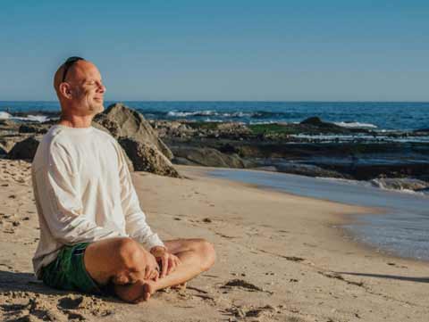 A man sitting cross-legged and meditating on a beach.